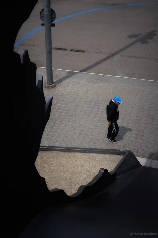 Gekaderde compositie met voorbijlopende man met blauwe petje en een blauwe boog op de straat. Centrum, Barcelona
