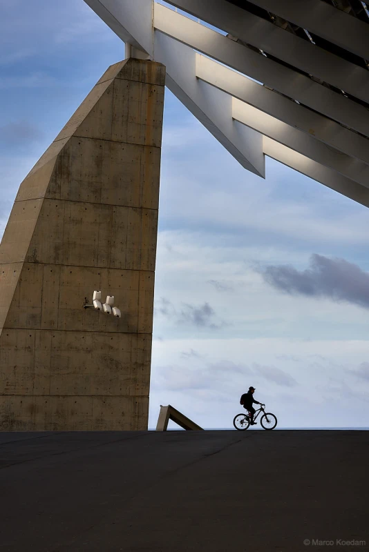 Silhouette van fietser in kader van grote architectonische elementen. Kust, Barcelona